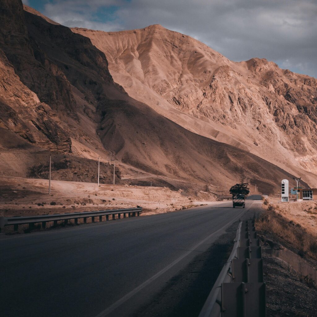 Remote highway cuts through dramatic, arid mountain landscape under cloudy skies.