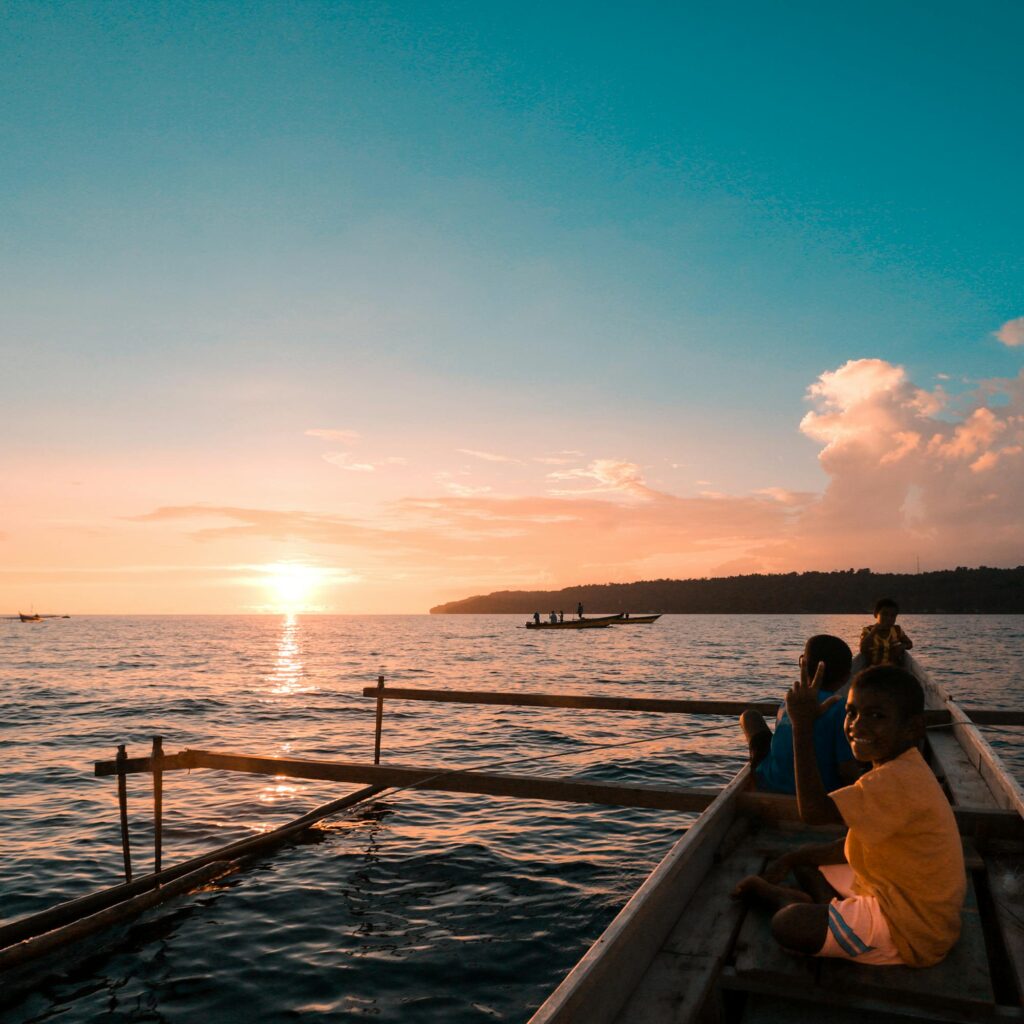 Children enjoying a boat ride at sunset in Yendidori, Papua, Indonesia, showcasing adventure and scenic beauty.