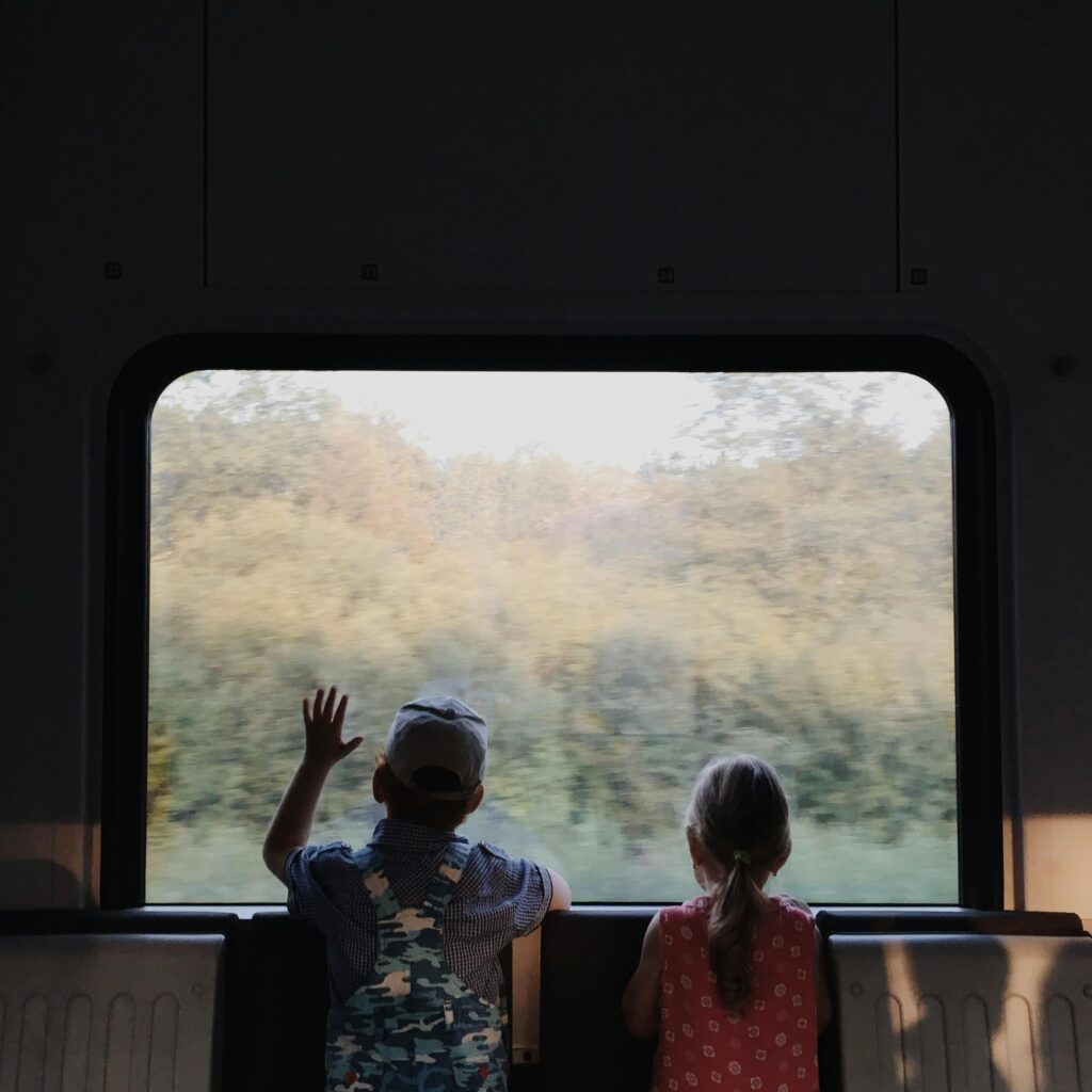 Two children gaze outside a train window, enjoying a journey through the Belarusian countryside.