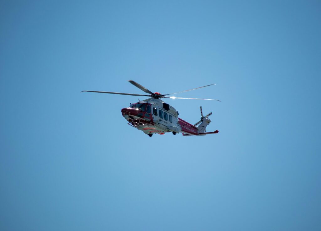 Red and white helicopter in flight against a cloudless blue sky, showcasing aviation technology.